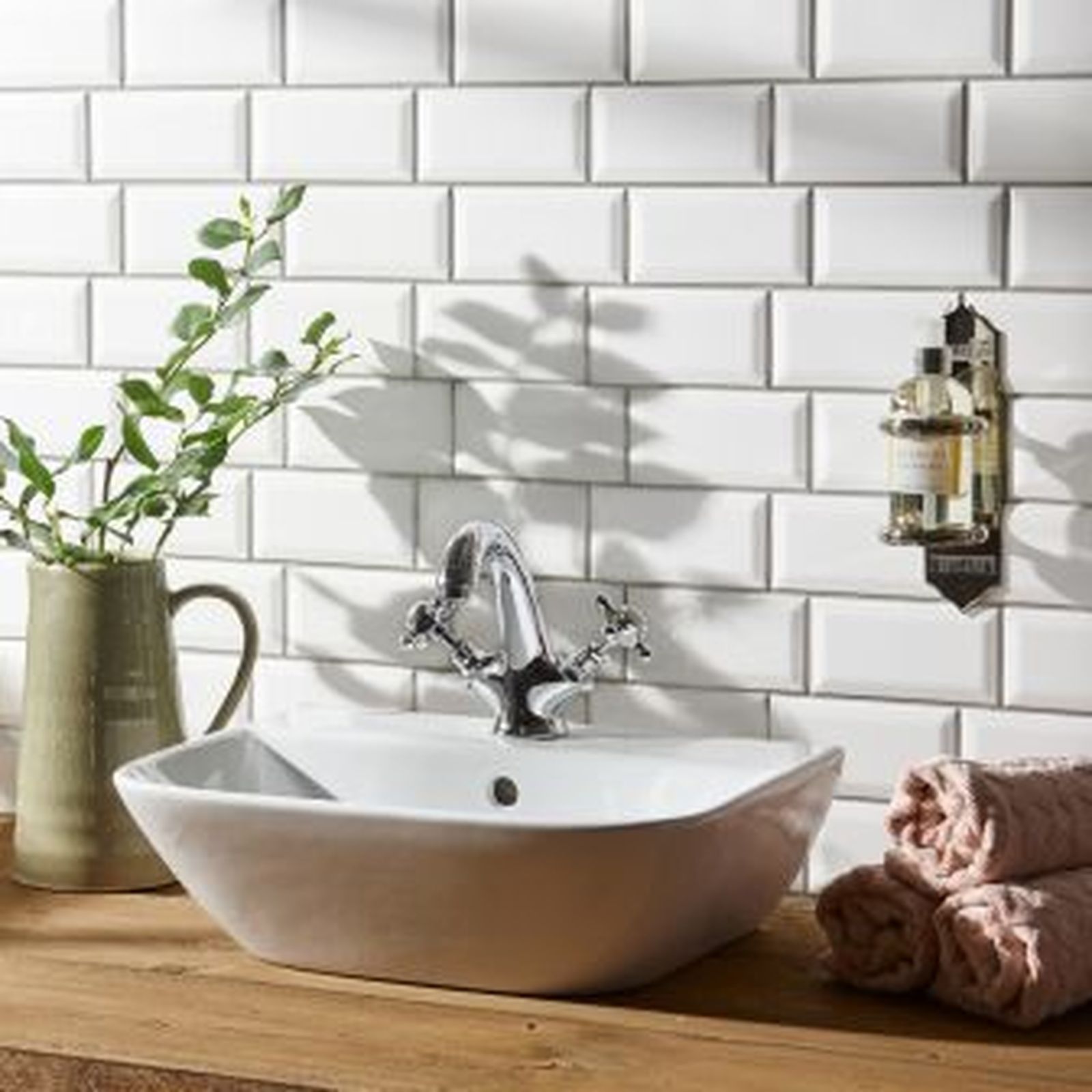 White tiled wall with a sink, faucet, and towels. Soap bottles hang on the wall.