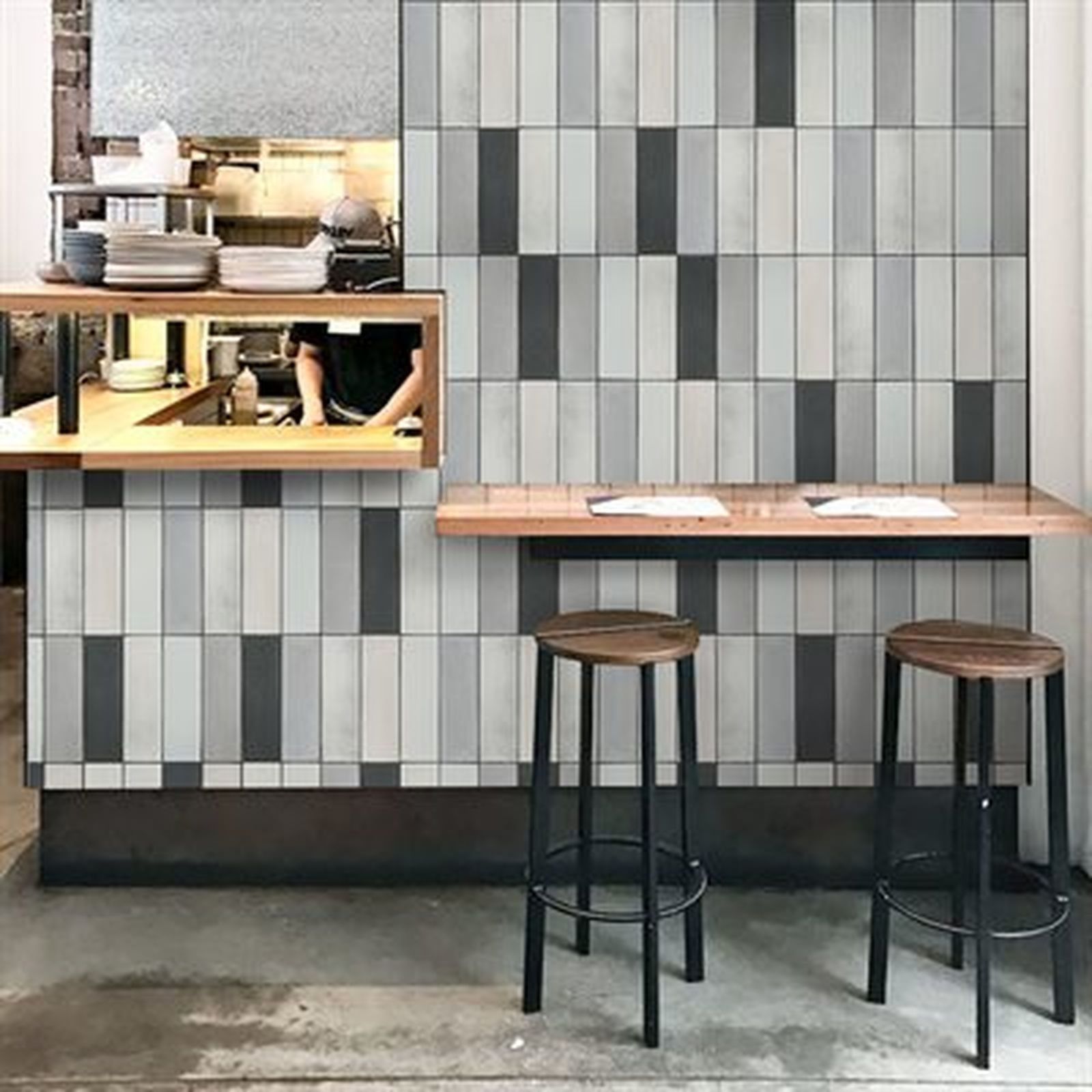 Cafe interior with a tile wall in gray and black, wooden bar and stools.