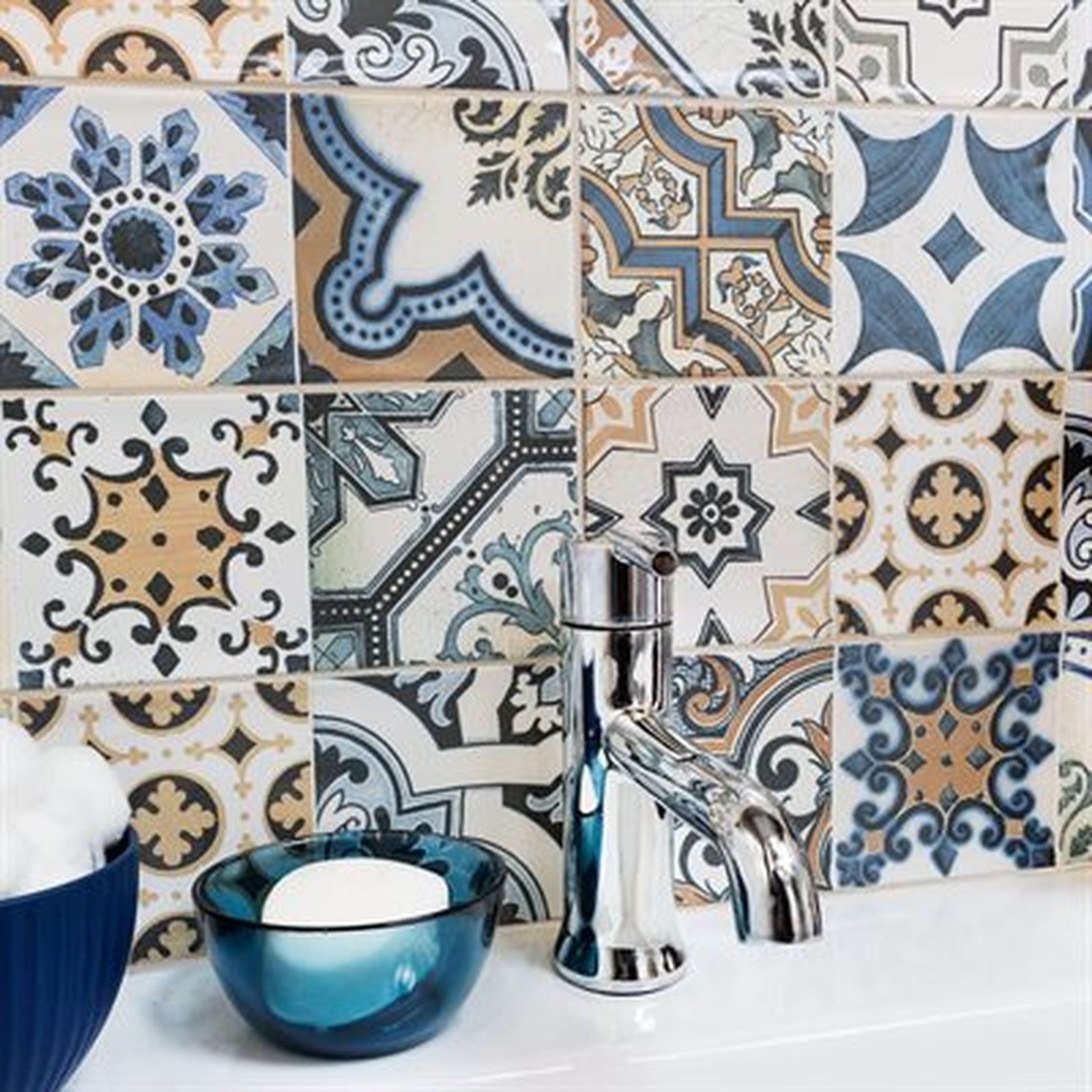 Close-up of a bathroom counter with patterned blue, white, and tan tiles, a chrome faucet, and a blue bowl with soap.