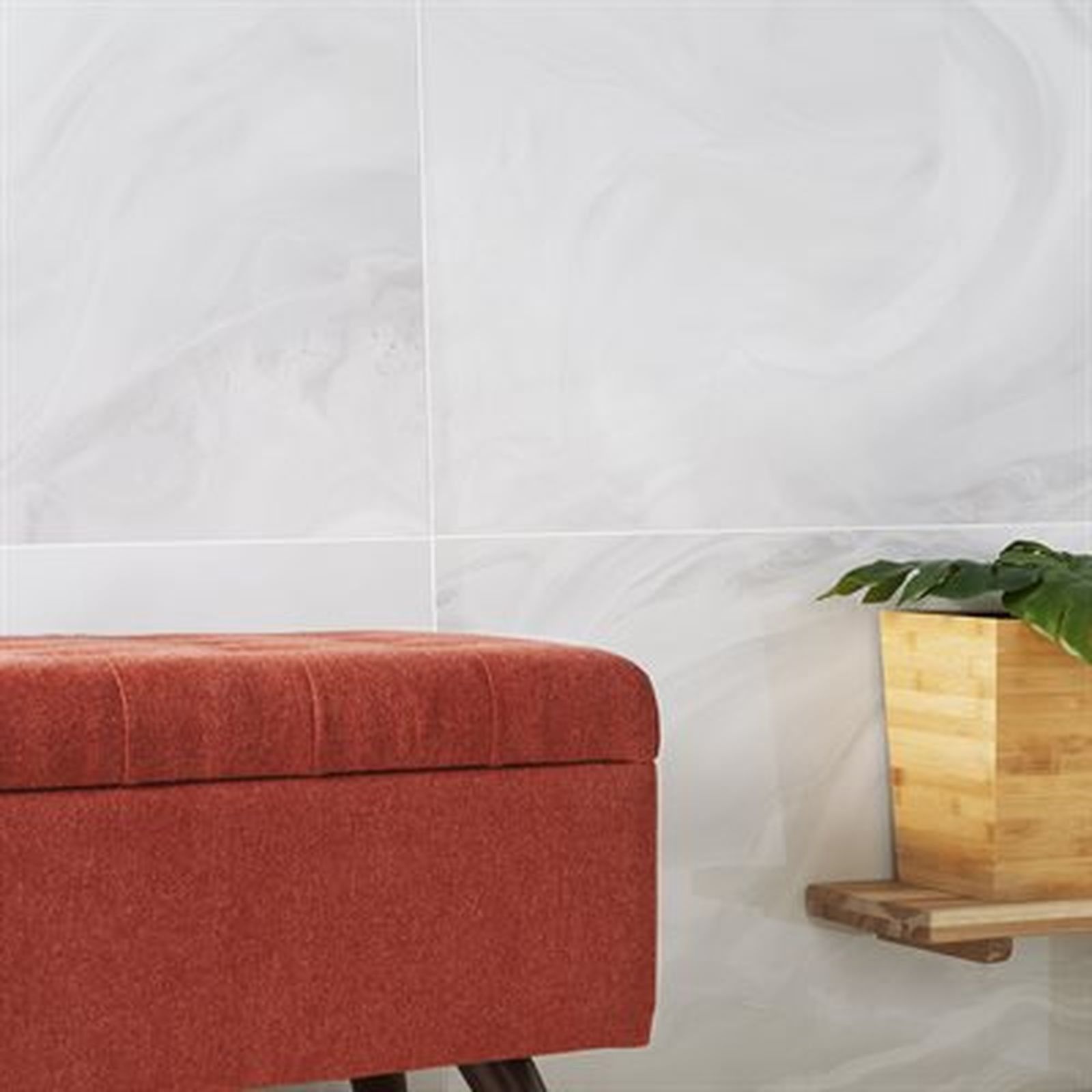 Red ottoman against white swirling-patterned wall, wooden shelf with plant.