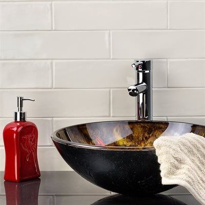 Bathroom sink with a glass bowl, chrome faucet, white tiled wall, red soap dispenser, and a towel.