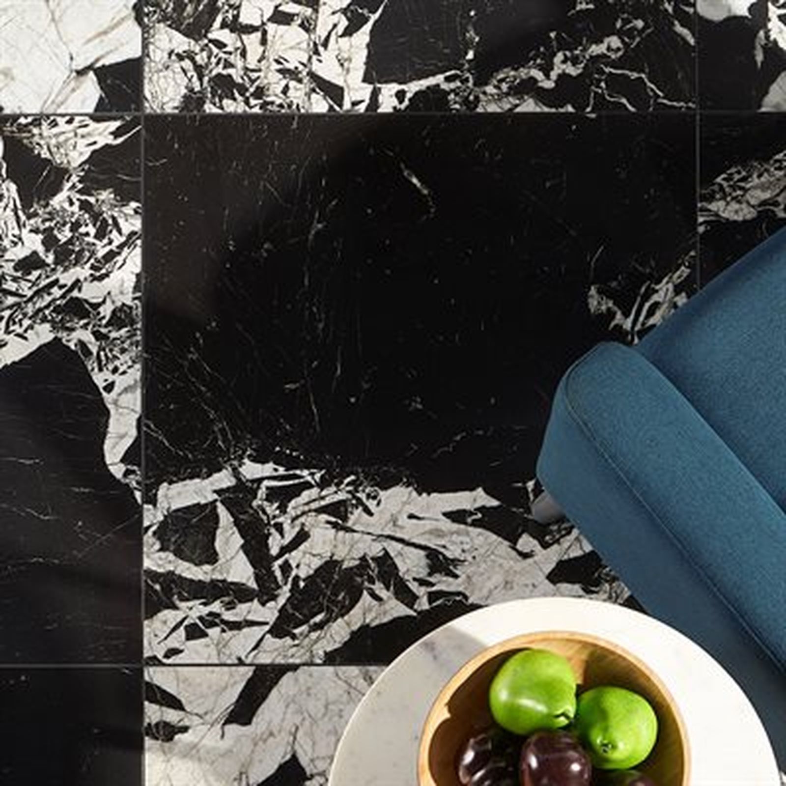 Close-up of marble tile floor, black square tile with a blue armchair and a bowl of fruit.