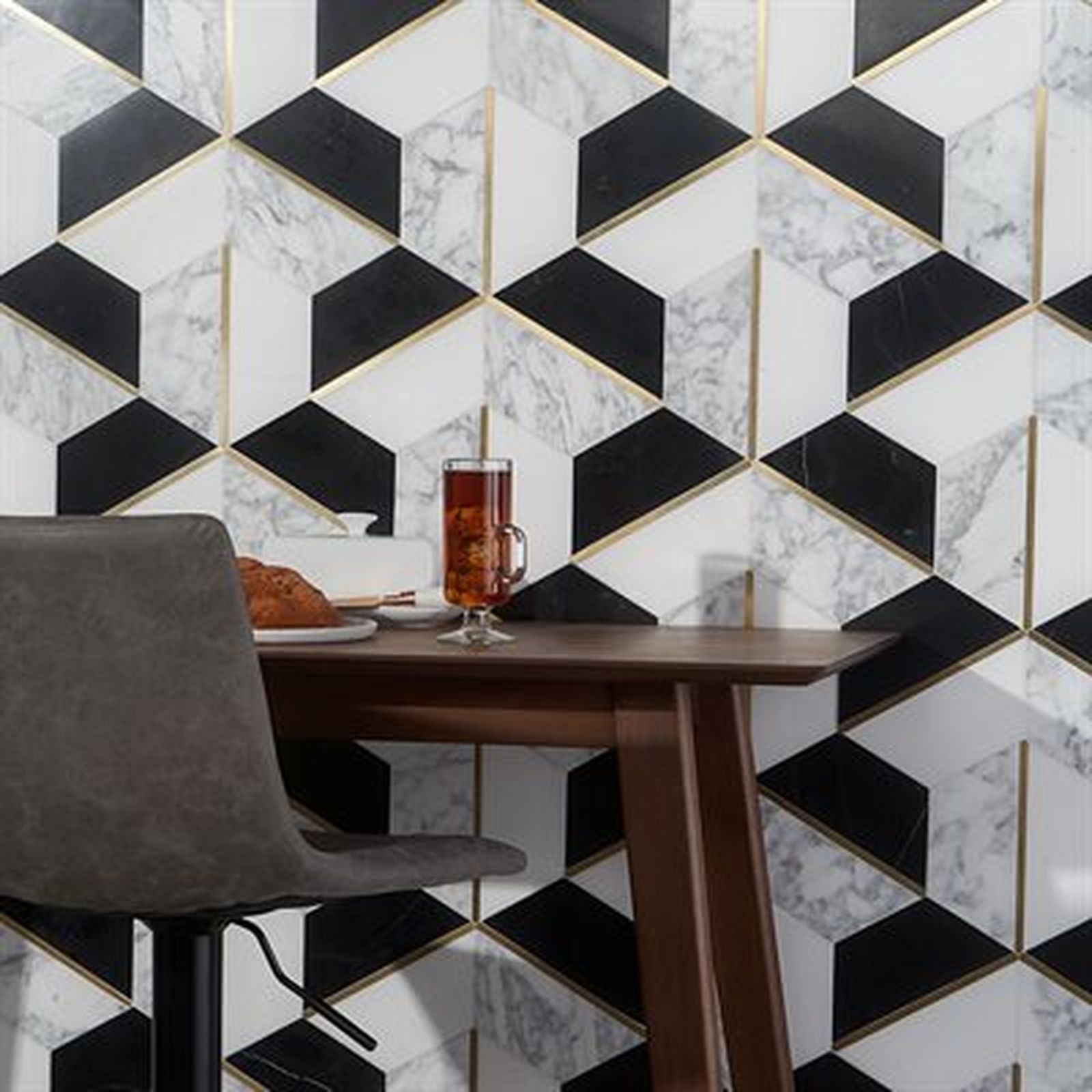 Geometric black/white tiled wall with gold trim, a dark table, and a grey chair.
