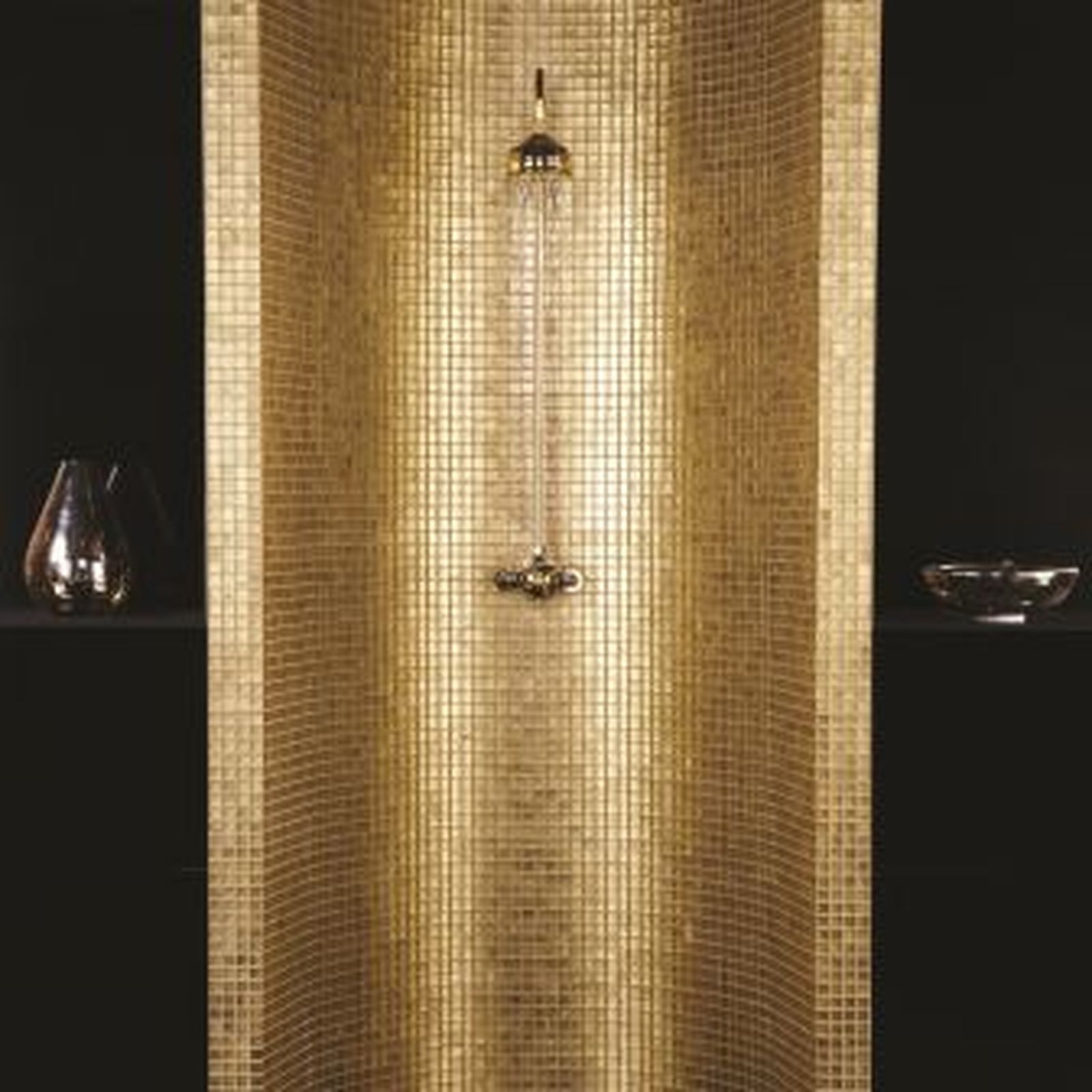 Golden mosaic-tiled shower with a curved back. Showerhead and controls are gold. Black shelves with decorative vases.