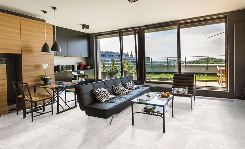 Modern living room with kitchen, black leather sofa, large windows, and a city view.