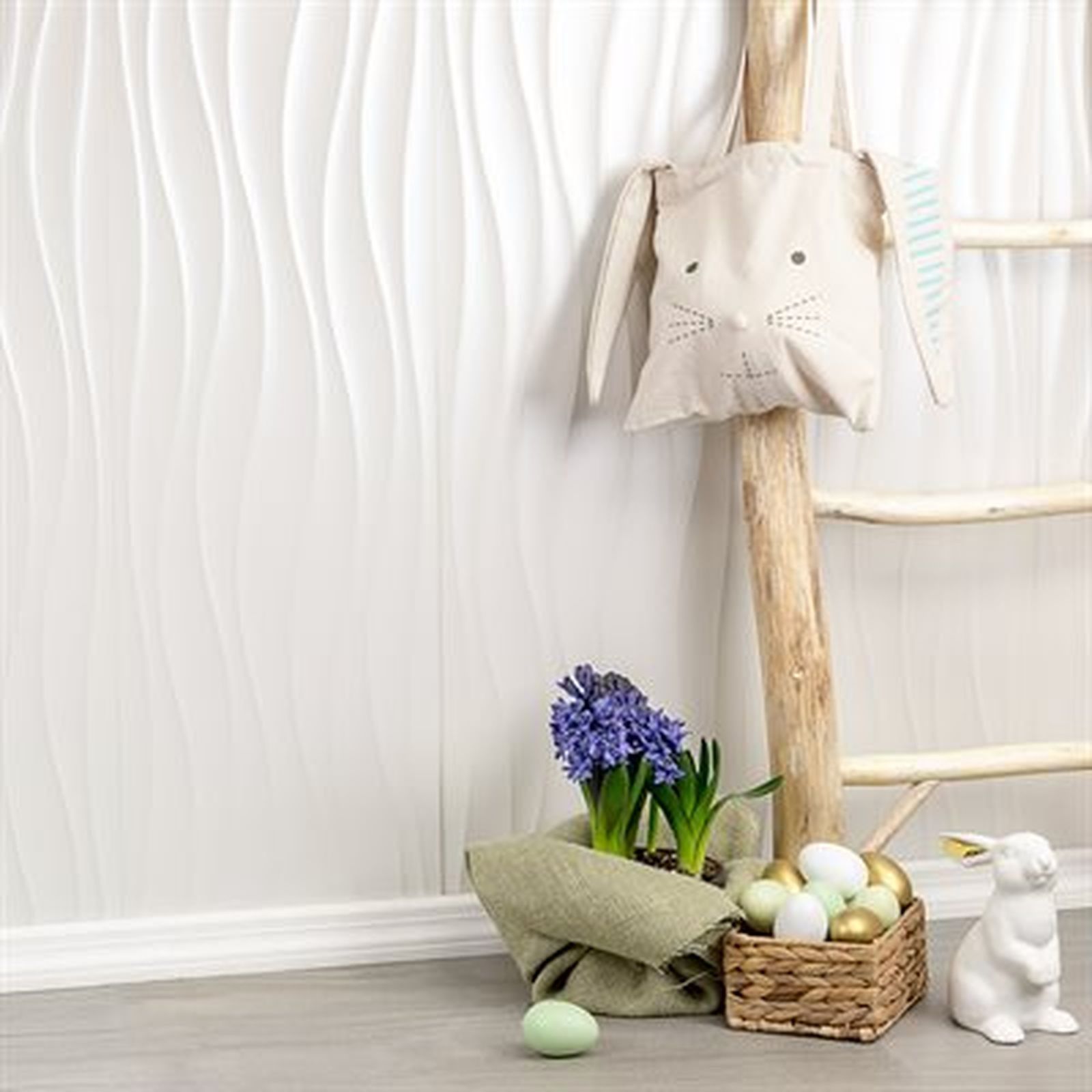 White wavy wall with Easter decorations: bunny bag, flowers, basket of eggs, ceramic bunny.