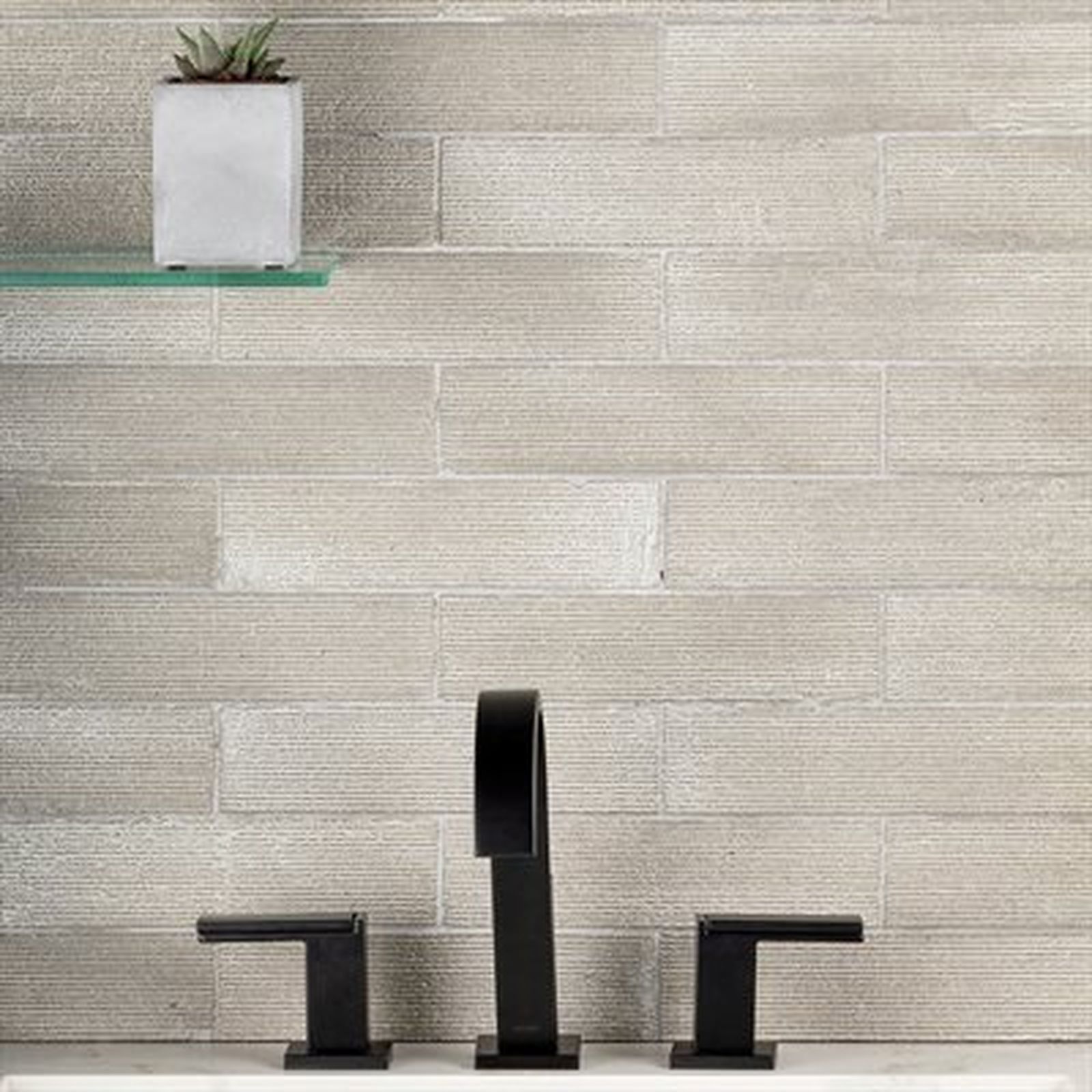 Bathroom sink with black faucet against a textured, light gray tiled wall. A small succulent plant sits on a glass shelf.