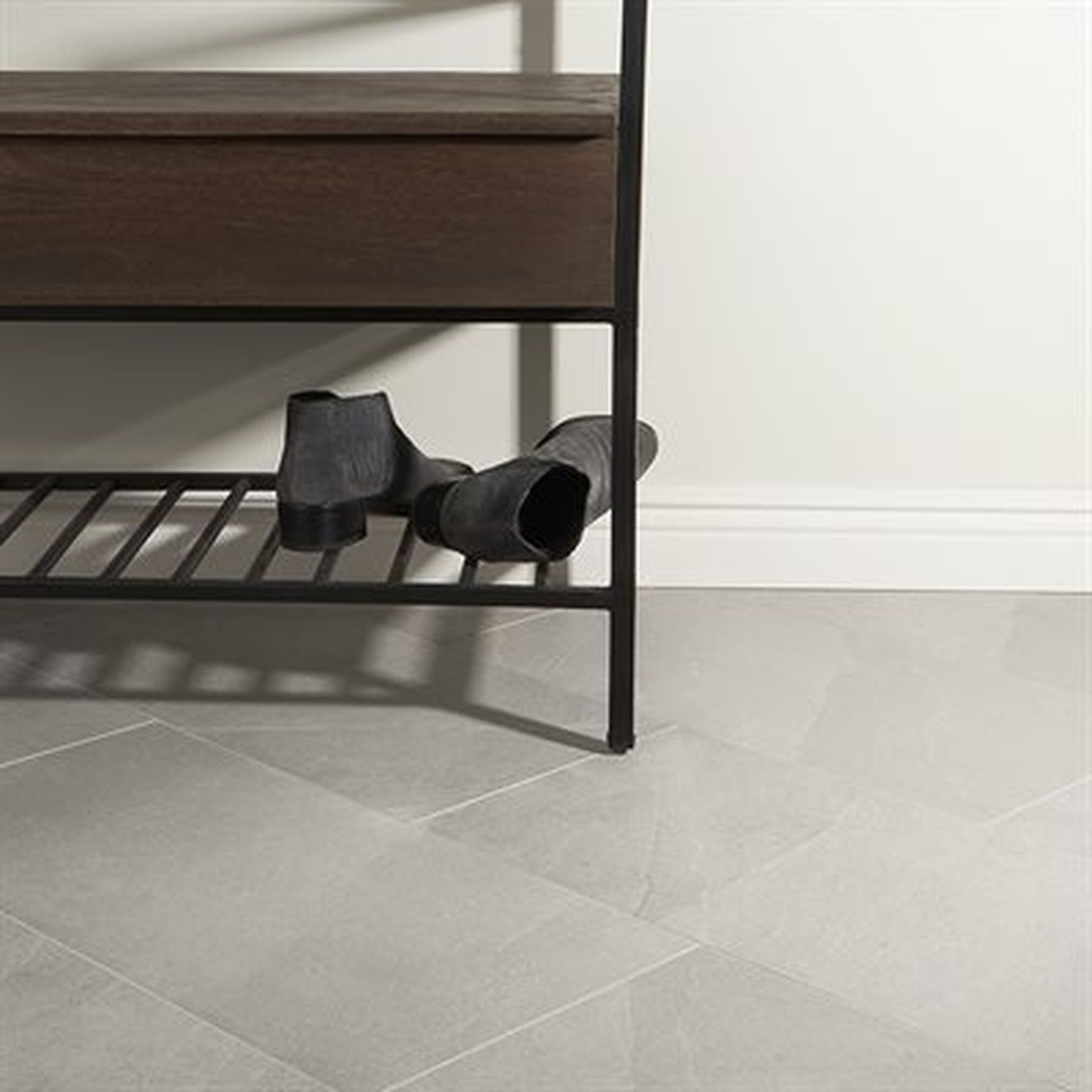 Gray floor tiles with a dark wooden shoe rack and black ankle boots.