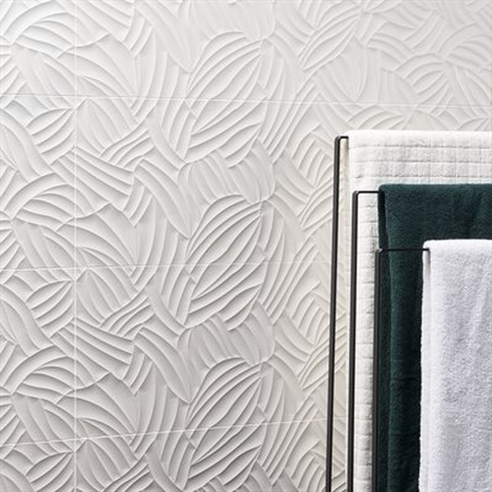 Textured white tile wall with a leaf pattern, beside a towel rack with green and white towels.