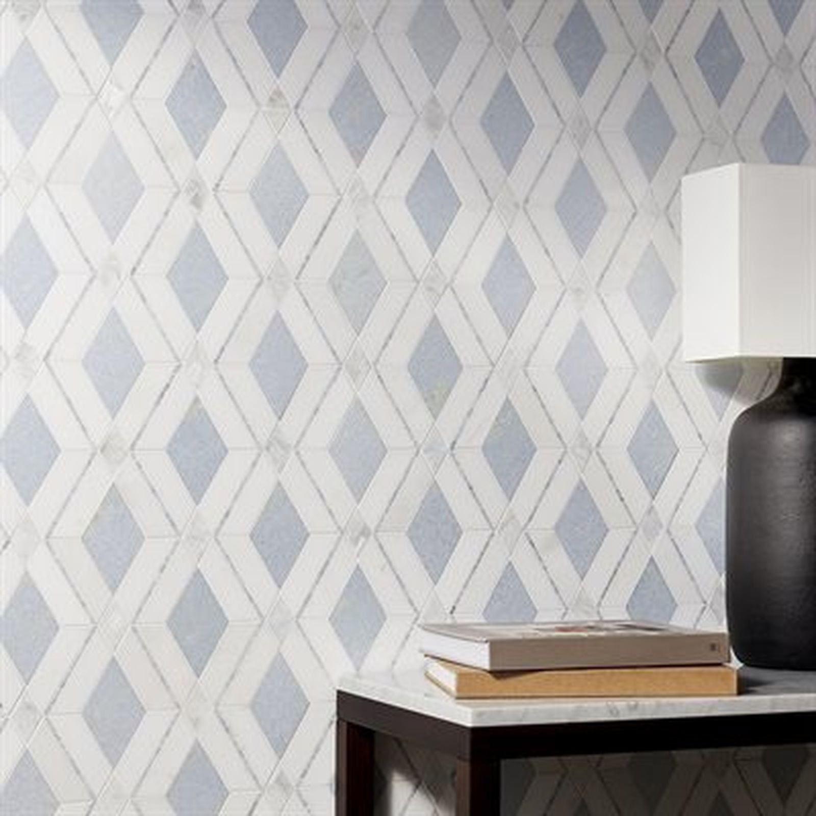 Wall of diamond-patterned tile in light blue and white behind a side table with books and a lamp.