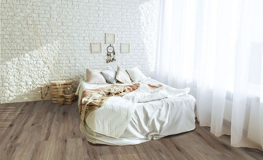 Bedroom with a white brick wall, bed with white bedding, and light wood flooring.