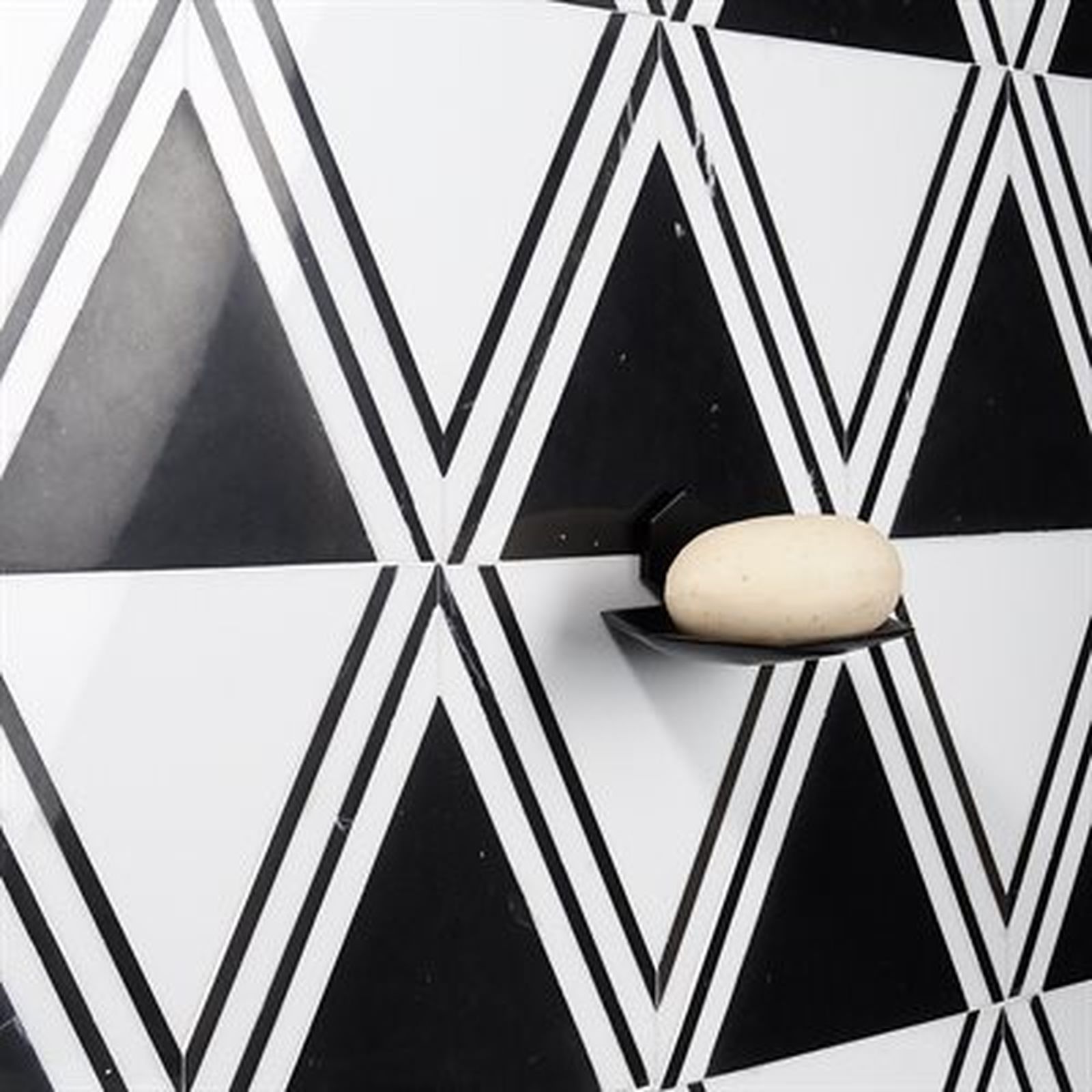 White soap on a black soap dish against a black and white triangle-patterned wall.