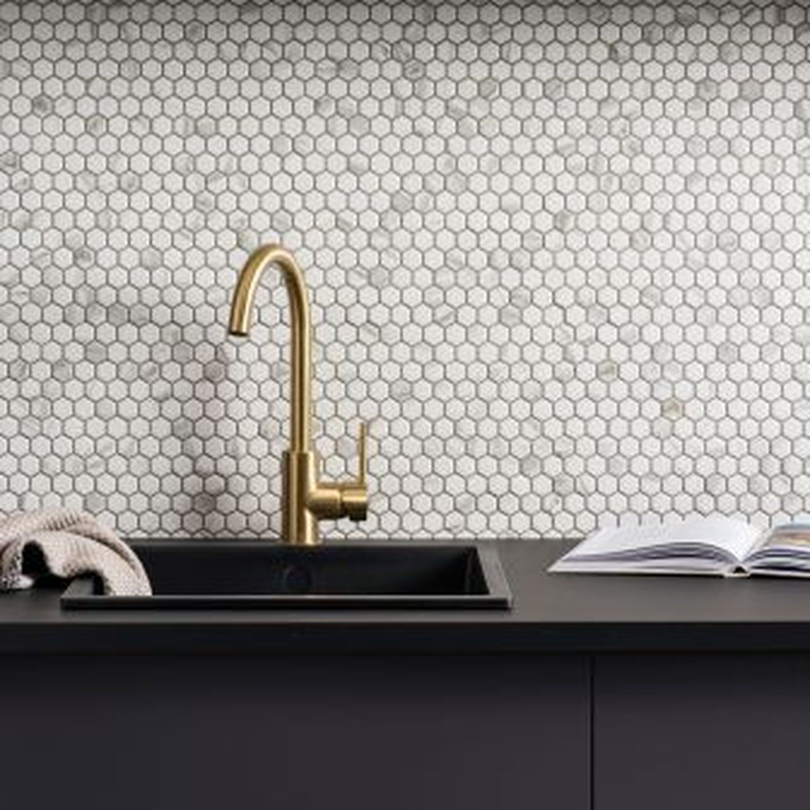 Gold faucet over black sink and countertop with marble hexagon tile backsplash.