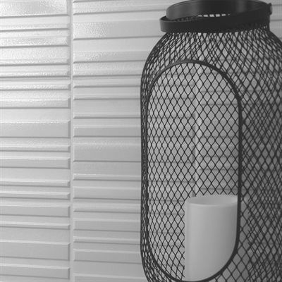 Black metal lantern with a white candle on a textured white wall.
