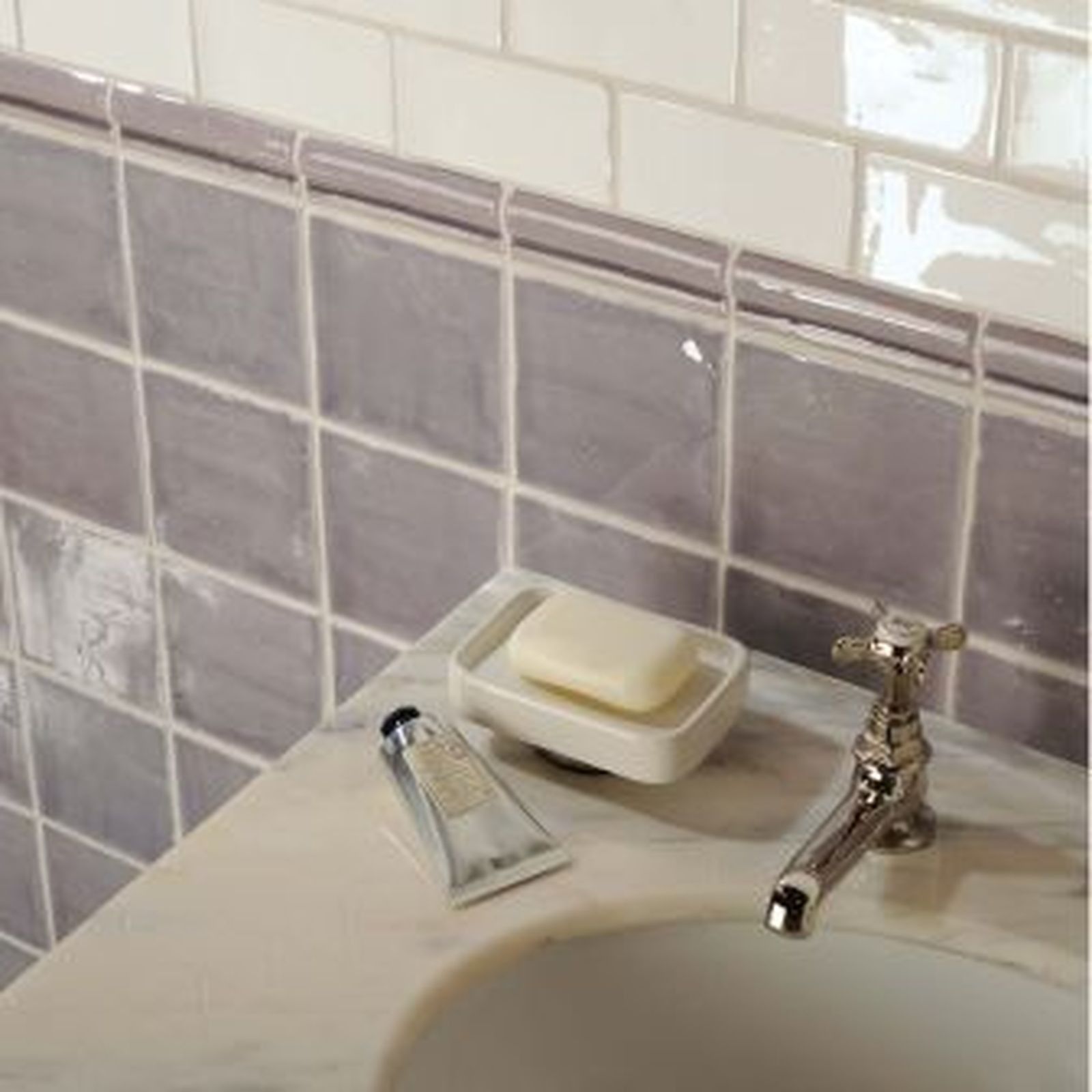 Bathroom with gray and white tile, marble countertop, and chrome faucet. Soap and lotion visible.