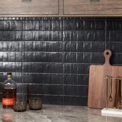 Black textured tile backsplash with wooden cabinets and accessories in kitchen.