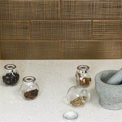 Spices in jars and mortar on a speckled countertop against a textured brown backsplash.