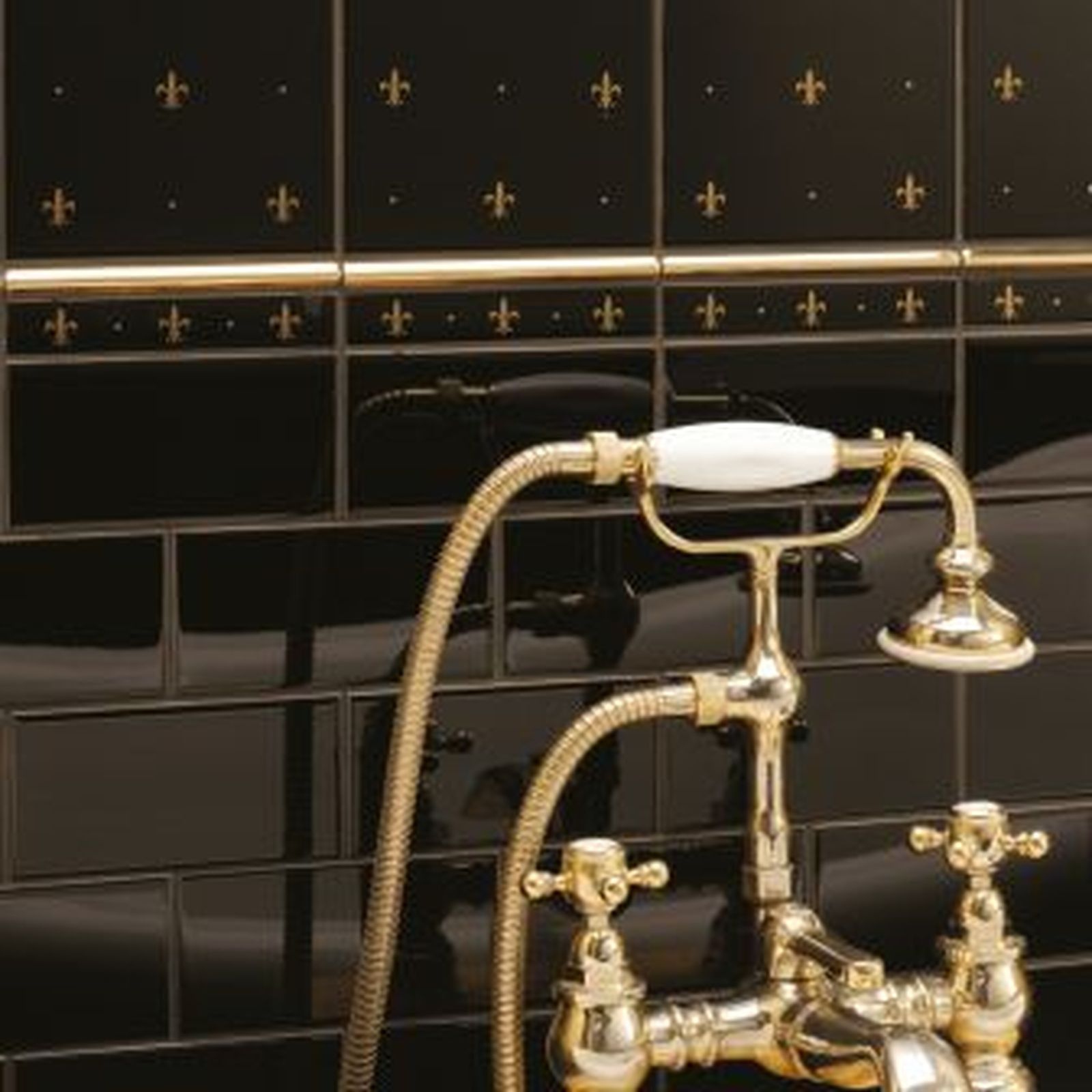 Gold-toned bathroom faucet with a white handle against black tile with gold fleur-de-lis accents.