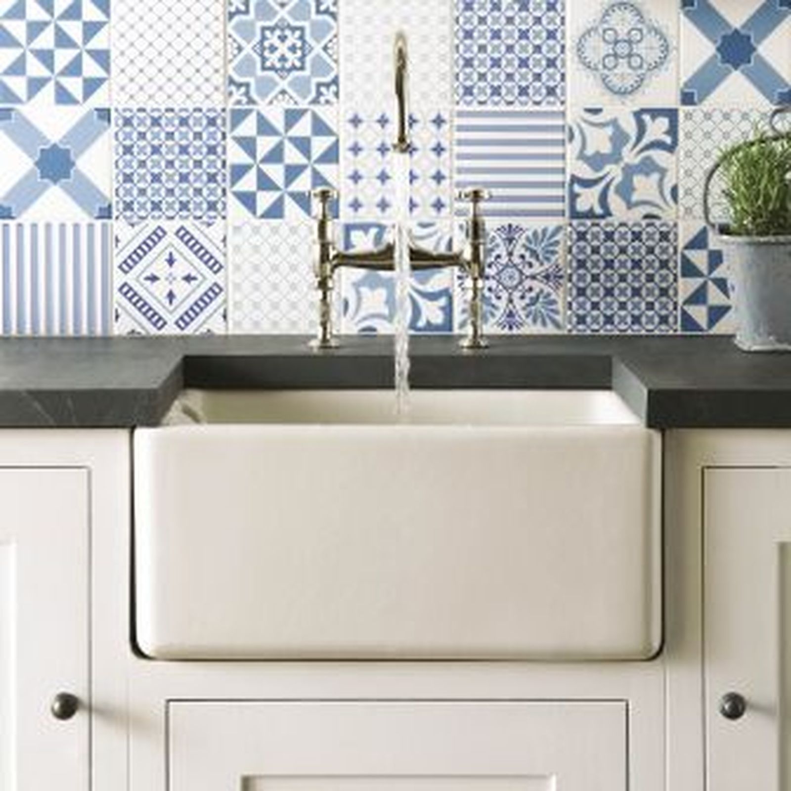 White farmhouse sink with water flowing, set against a blue and white patterned tile backsplash.