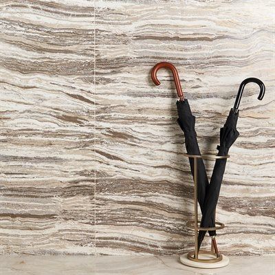 Two black umbrellas in a gold stand against a wall with layered brown and beige tones.