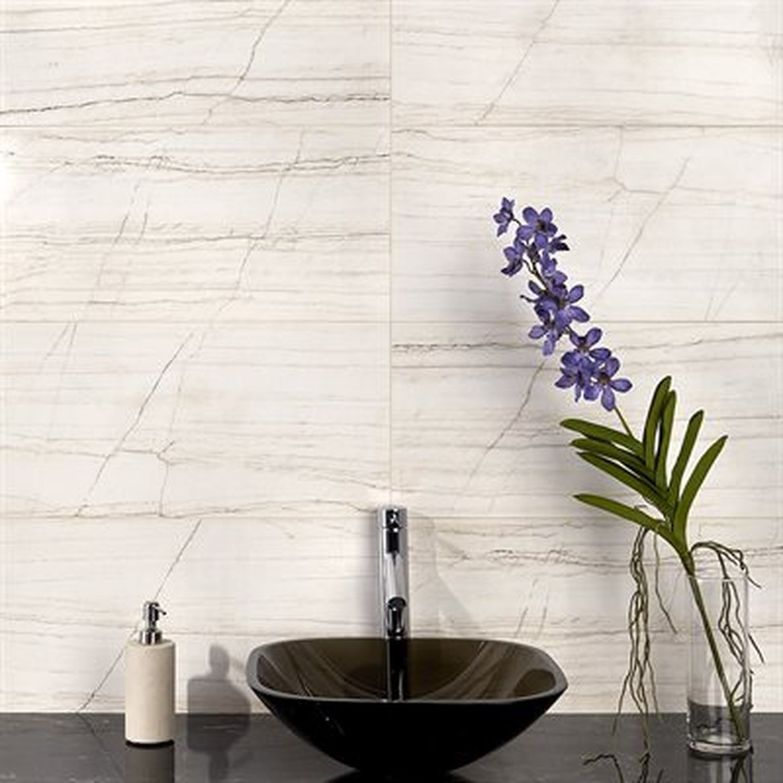 Bathroom with marble-look wall tiles, black sink, silver faucet, soap dispenser, and purple flowers in a vase.