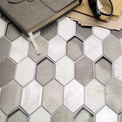 Close-up of a honeycomb-patterned tile with shades of gray, white, and silver, with a notebook and glasses on top.