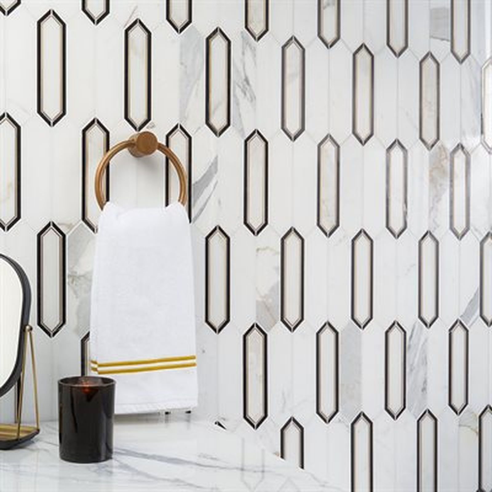 White and black tile bathroom wall with gold towel ring and white towel.