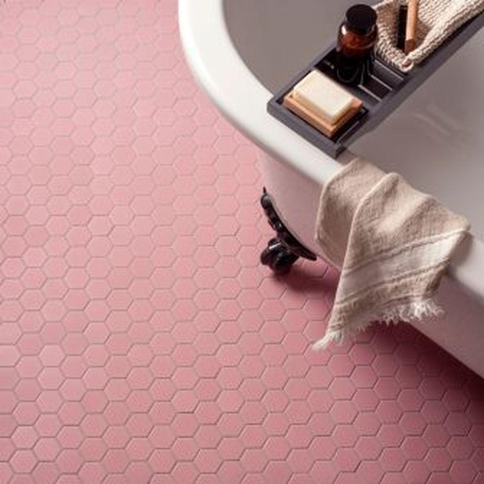 Pink hexagon tile bathroom floor with a white clawfoot tub and tray of toiletries.