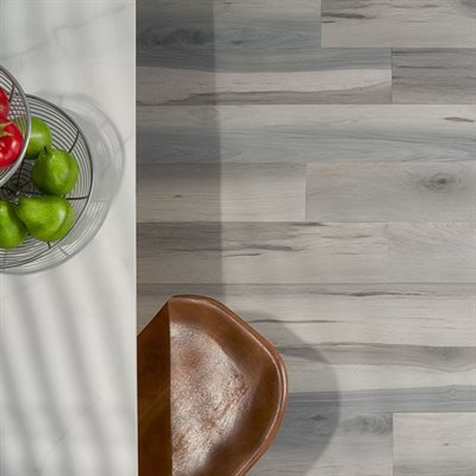 Top-down view of kitchen with a bowl of fruit, a leather chair, and light grey wood-look flooring.