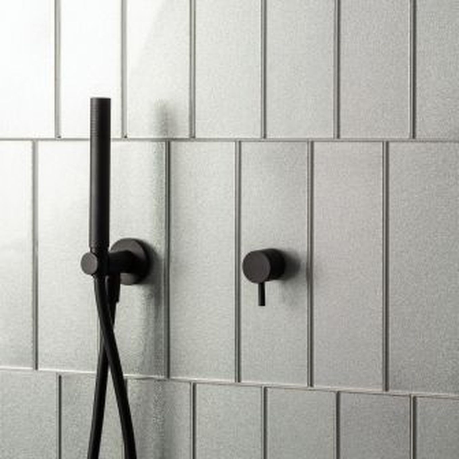 Black shower fixtures on vertical gray tiled wall.