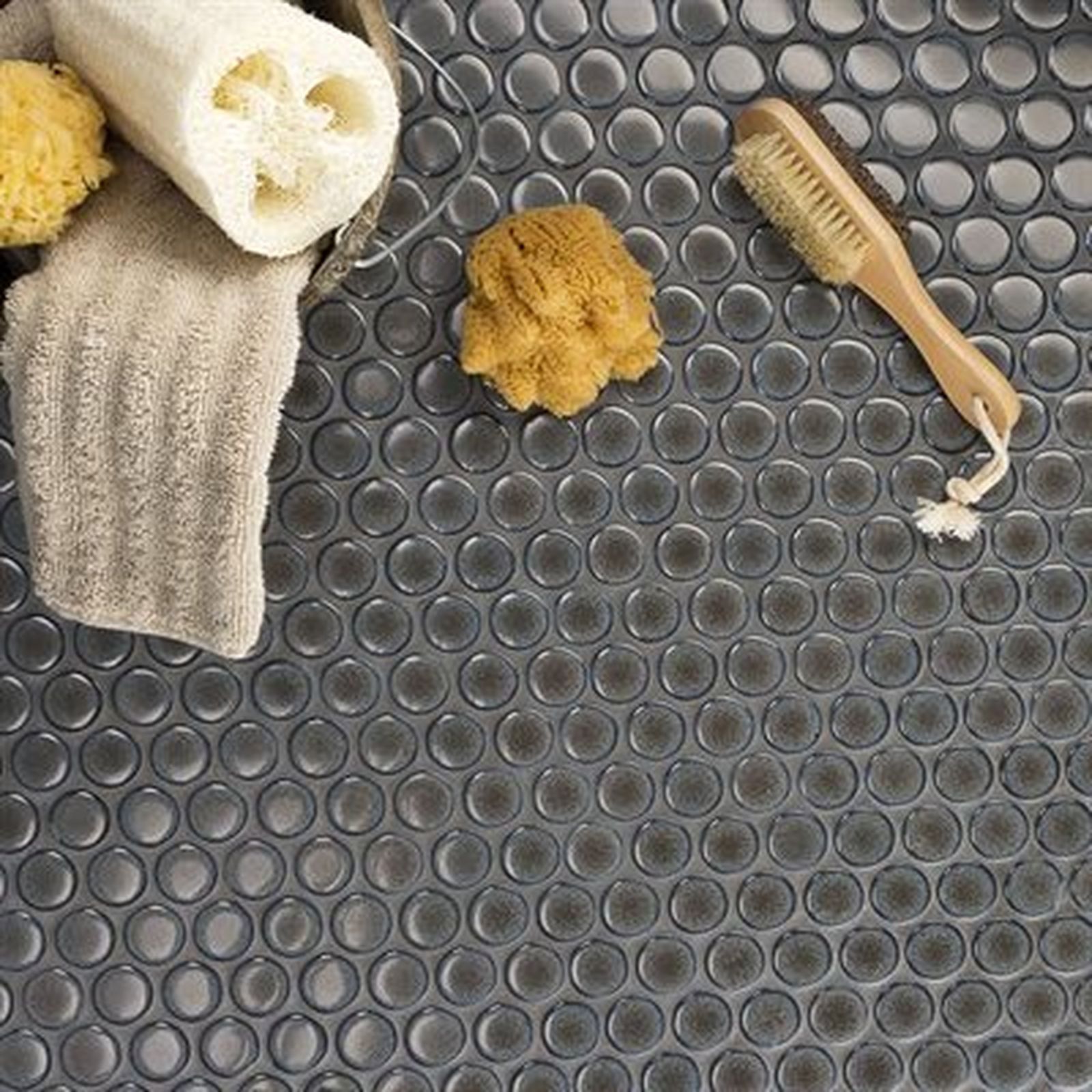Bath accessories on a dark, circular tile surface: sponge, brush, washcloth, and loofah.
