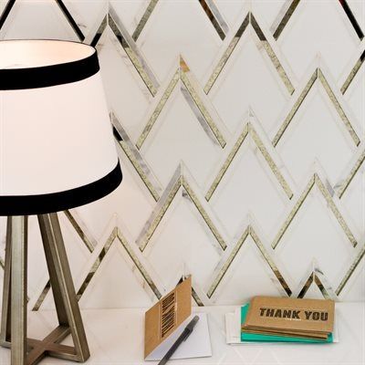 Lamp on desk next to white, gold, and mirrored chevron tile. Thank you card and pen on desk.