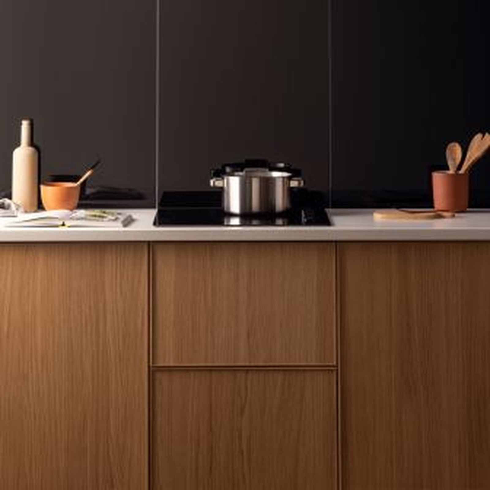 Kitchen with wooden cabinets, white countertop, black backsplash, and cooking pot on the stovetop.