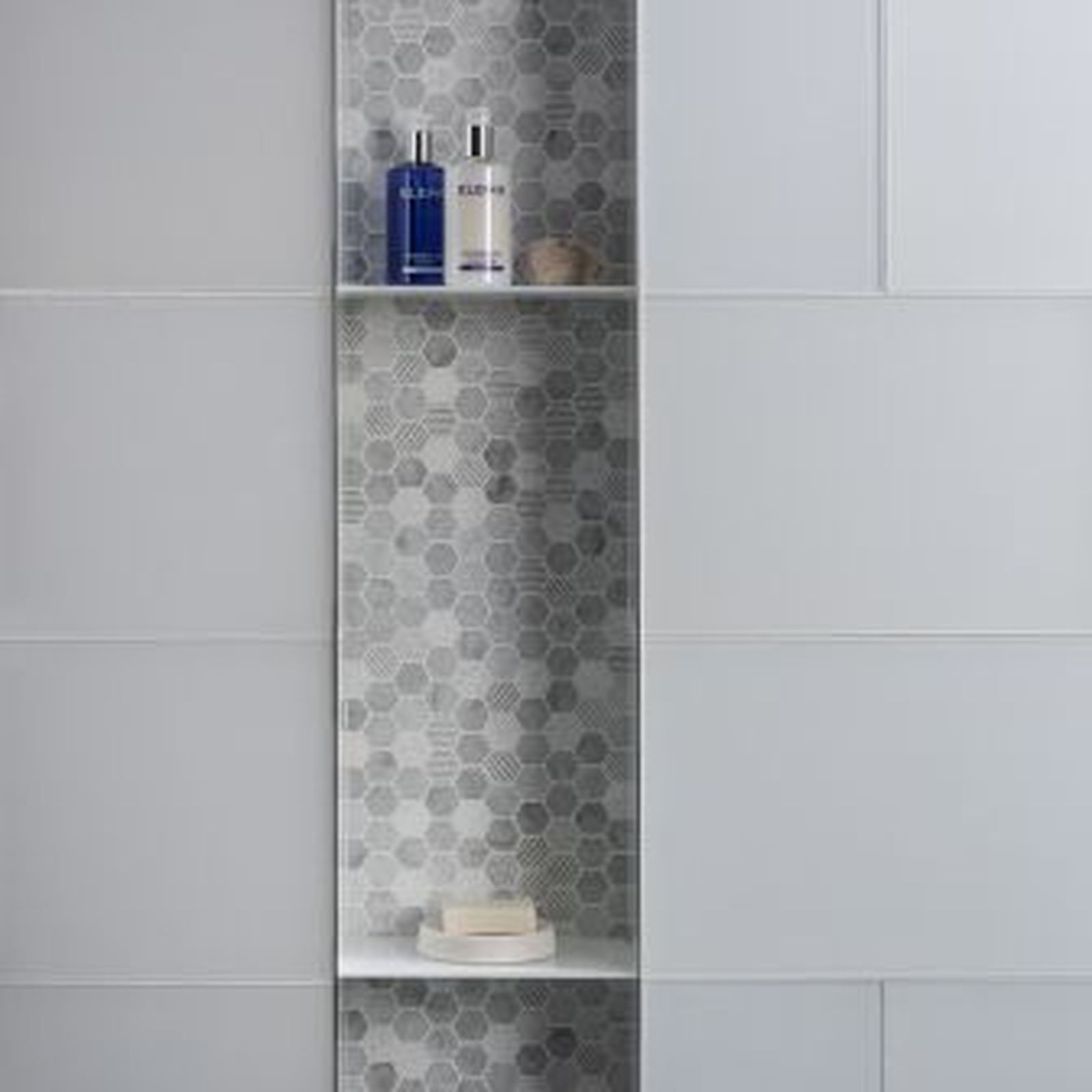 Bathroom wall with a recessed shelf filled with toiletries, gray and white tile.