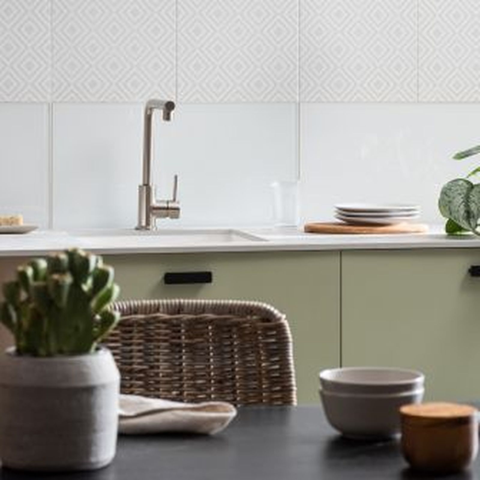 Kitchen with sage green cabinets, white backsplash with diamond pattern, and stainless steel faucet.