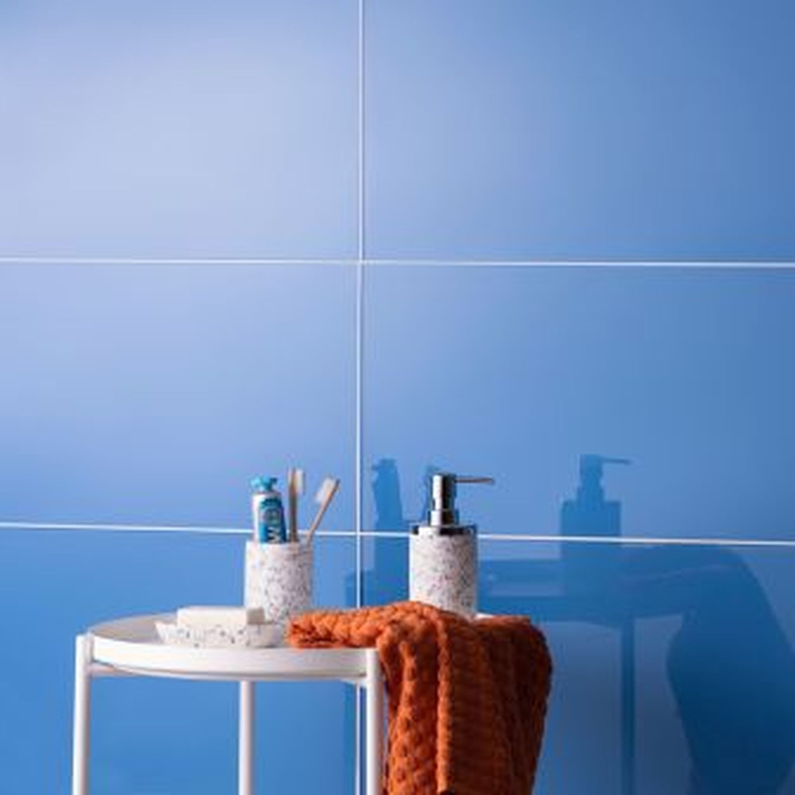 Blue-tiled bathroom with a white side table holding toiletries and an orange towel.