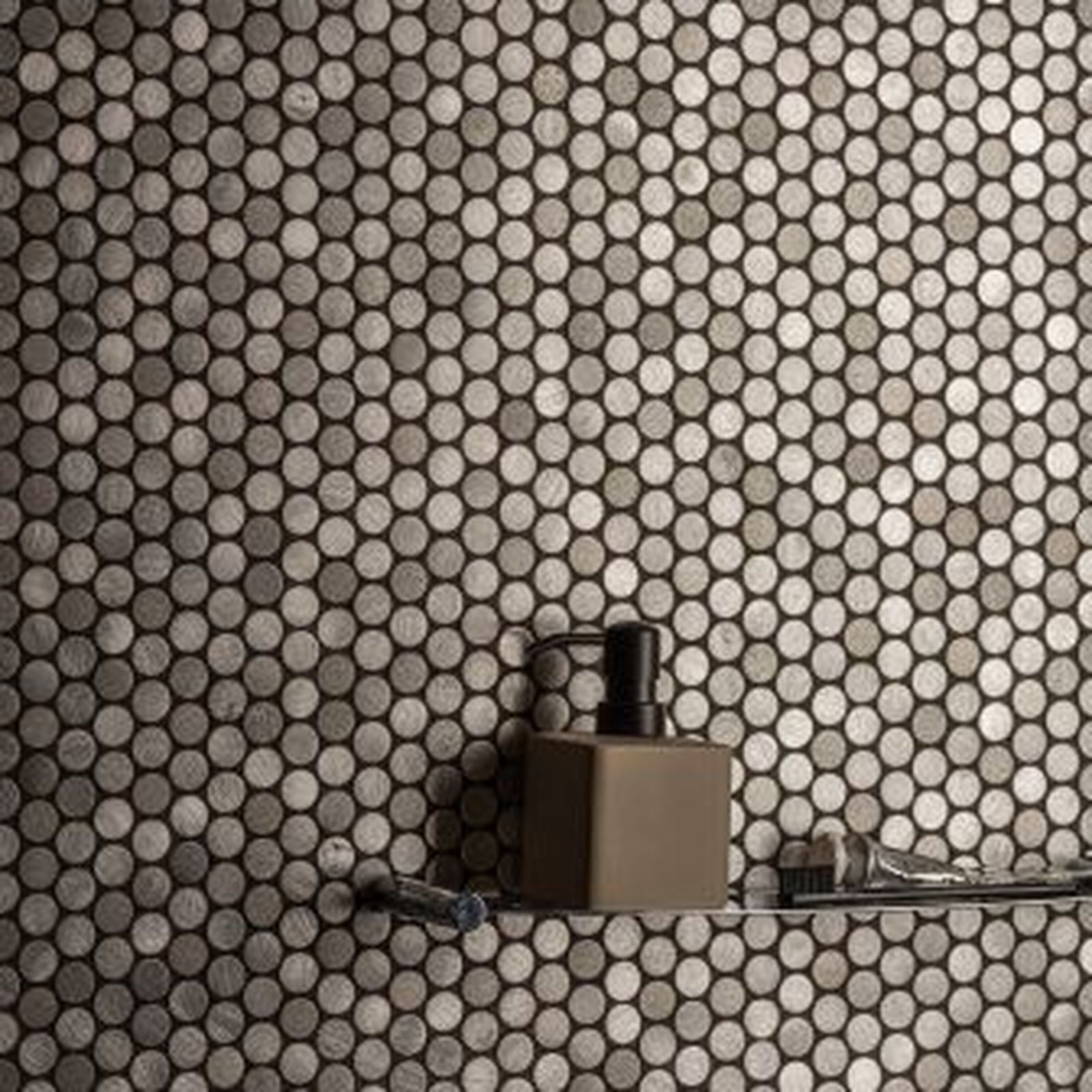 Shelf with dispenser and toothbrush against a mosaic tile wall with small, round, gray tiles.