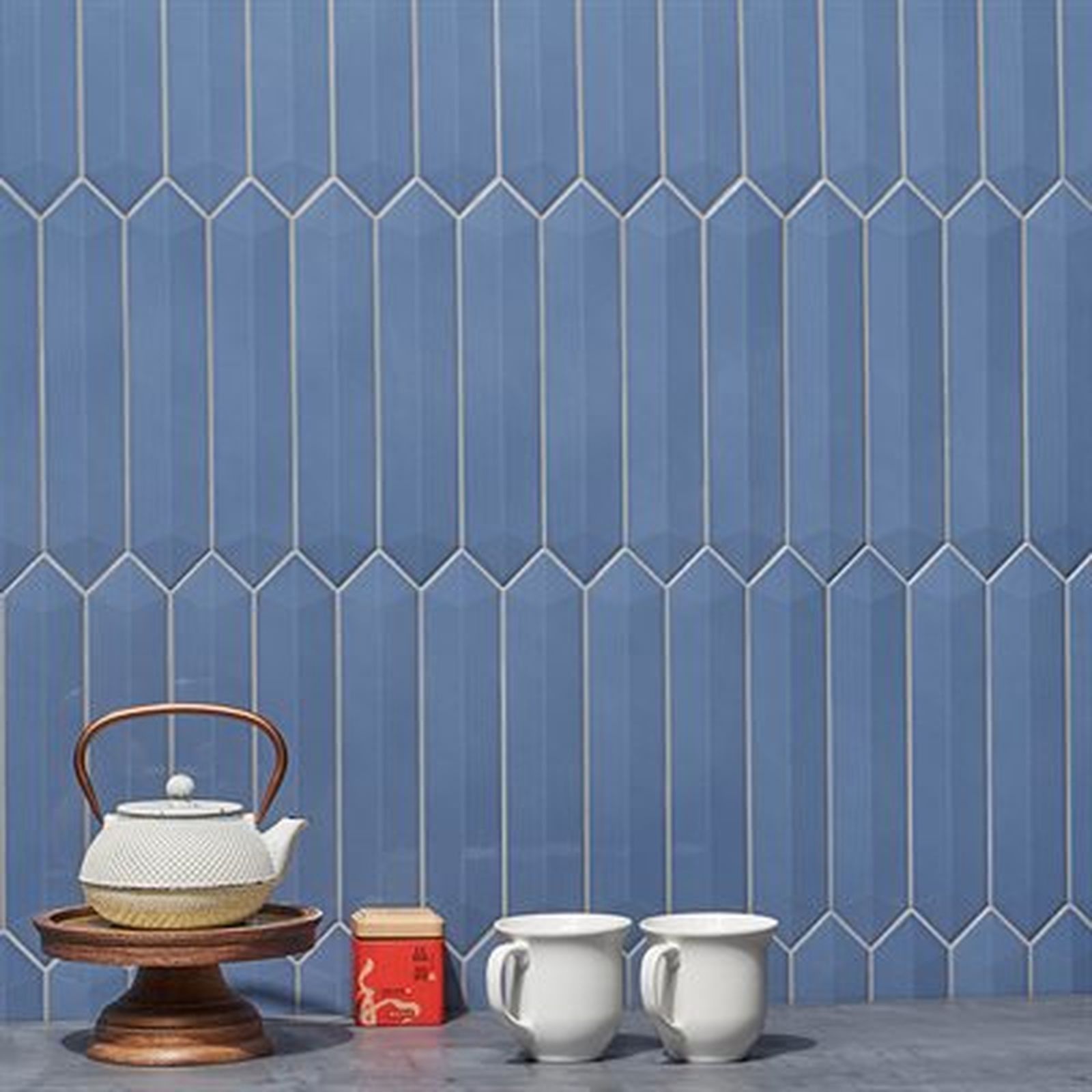Blue, spear-shaped tiled wall with tea set on a wooden stand, two mugs, and a small tin.