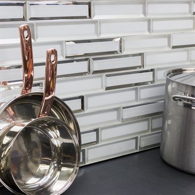 Copper-handled pots sit on a black countertop in front of a white and mirrored tile backsplash.