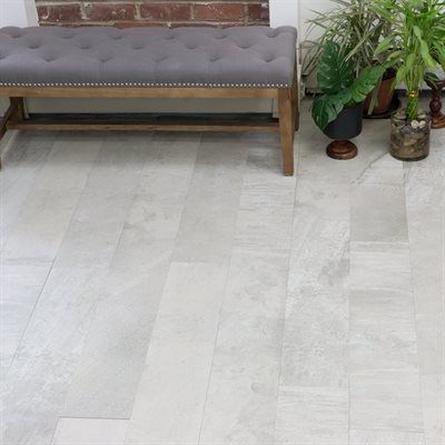 Gray tiled floor with a button-tufted bench and potted plants in a light-filled room.