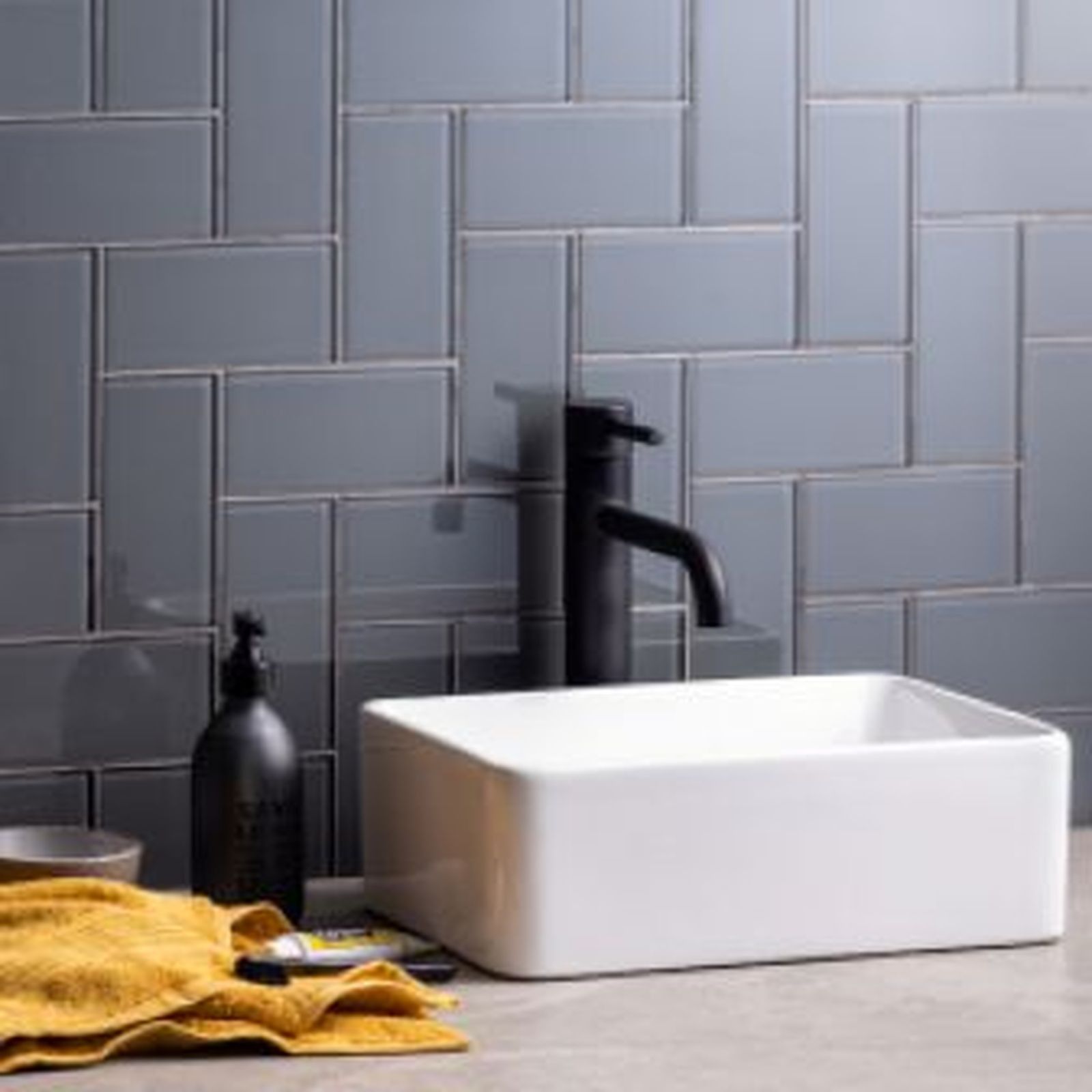 White rectangular sink with black faucet, soap dispenser, and yellow towel against gray tiled wall.