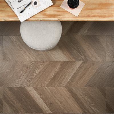 Overhead shot of desk with a chair and herringbone wood floor. Desk is light wood, chair is beige.