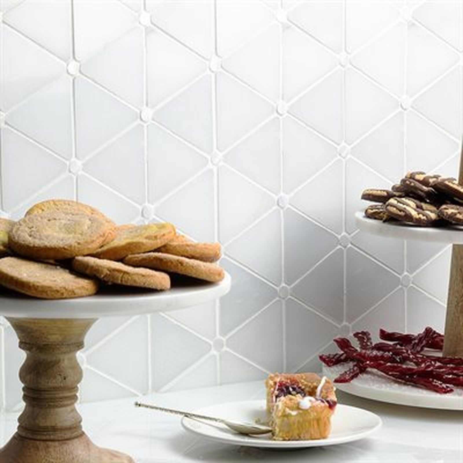 Cookies and pastries on cake stands, with decorative white triangular tile background.