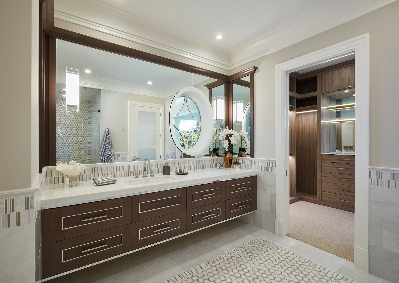 Bathroom with a large mirror over a dark brown vanity with white countertop. Walk-in closet visible.