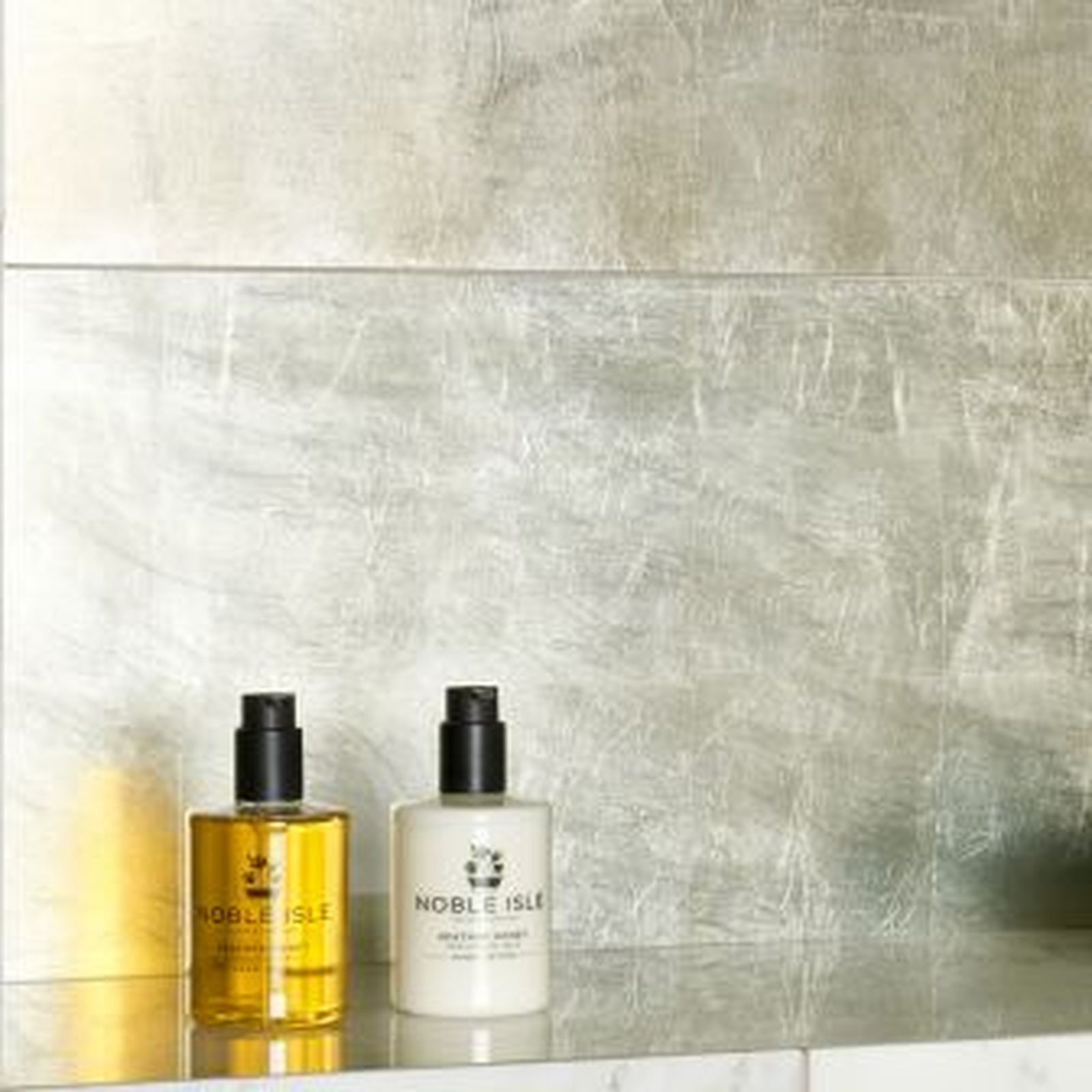 Two bottles of Noble Isle products on a shelf against a metallic silver-toned wall.