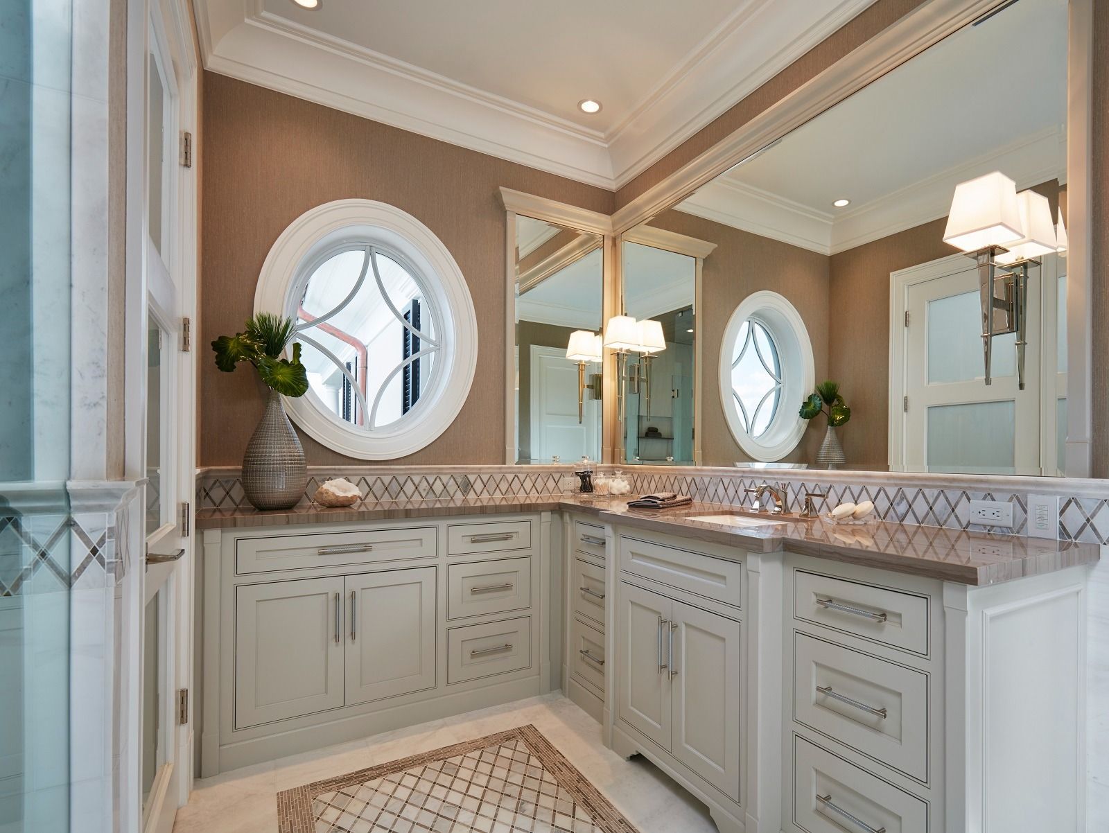 Bathroom with oval windows, beige walls, and light cabinets. Large mirror and stone countertops.