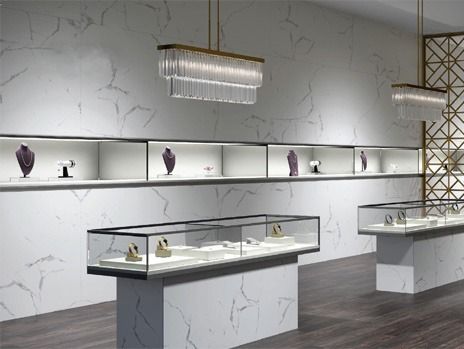 Jewelry store interior with illuminated display cases showcasing necklaces and watches; marble walls.
