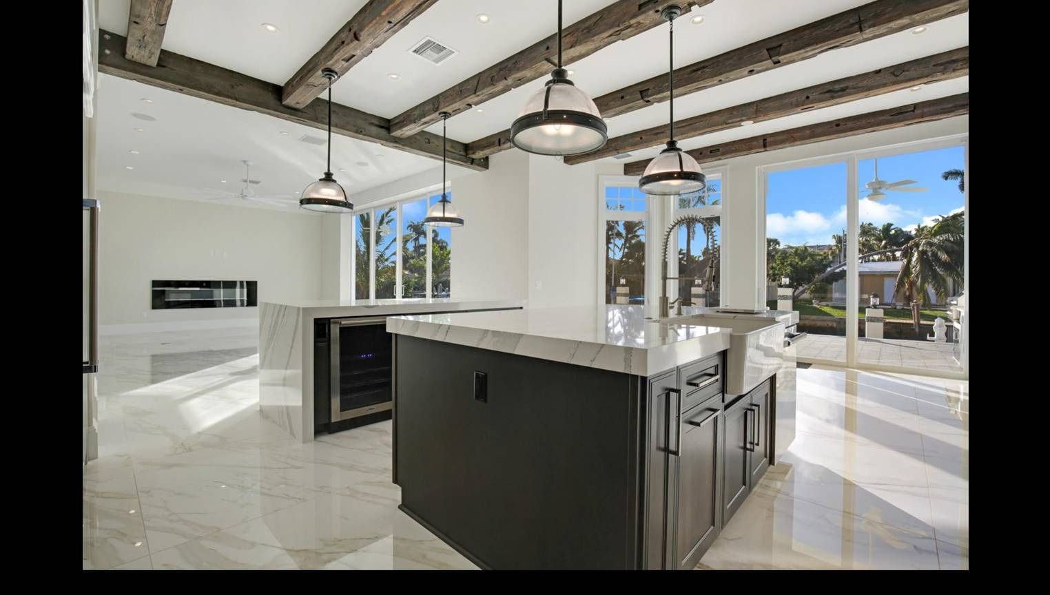 Modern kitchen with dark cabinetry, marble countertops, pendant lights, and large windows with a view.