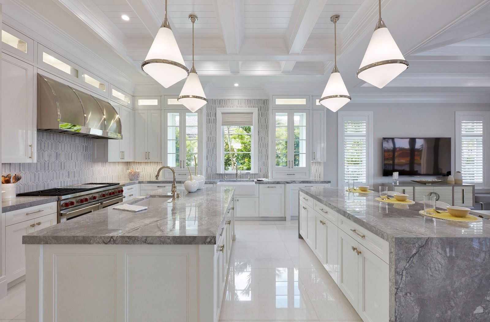 Modern white kitchen with two islands, pendant lights, and stainless steel appliances.
