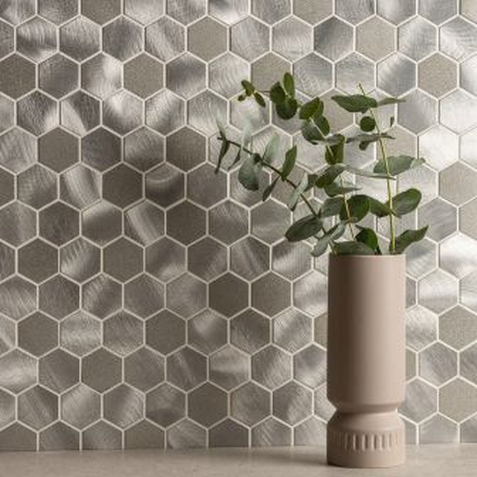Hexagonal silver-toned wall tiles with a vase holding eucalyptus branches.